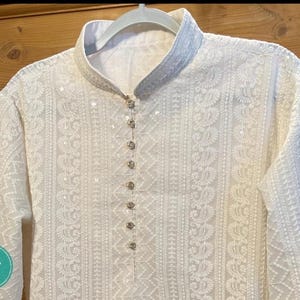 May include: White embroidered kurta with a button-up closure and long sleeves. The kurta is made of a delicate fabric and features intricate floral patterns.