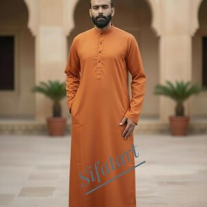 May include: An orange long-sleeved tunic with a mandarin collar and button-down front. The tunic has two front pockets and is ankle-length. The model is wearing brown sandals. The word "Sifart" is written on the tunic.