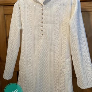 May include: White long-sleeved kurta with intricate embroidery and a button-up closure at the neckline.