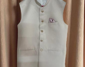 May include: A light beige vest with a mandarin collar and a pocket square. The vest has a button-down front with four buttons and two front pockets. The pocket square is a light purple color. The vest is hanging on a pink hanger.