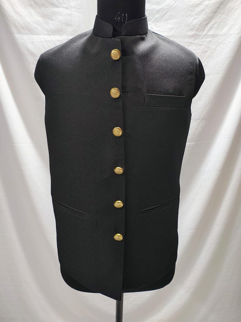 Puede incluir: Un chaleco negro sin mangas con cuello mandar&iacute;n y botones dorados.