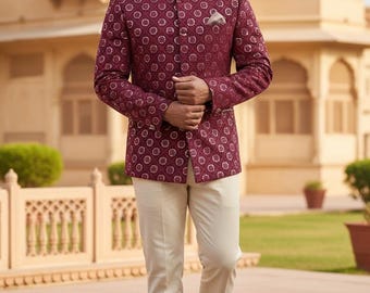 May include: A burgundy patterned jacket with a mandarin collar and matching pocket square, paired with cream-colored trousers and dark brown loafers. The outfit is worn in an outdoor setting with a stone walkway and a building in the background.