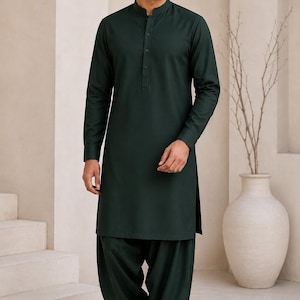 Peut inclure: Un kurta vert forêt foncé doté d'un col officier, d'une patte de boutonnage et de manches longues, associé à un pantalon plissé ample assorti. L'ensemble est complété par des chaussures à enfiler noires, créant un look monochrome cohérent.