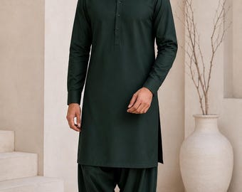Op de afbeelding: Een donker bosgroene kurta met een mandarijnkraag, een knoopsluiting en lange mouwen, gecombineerd met een bijpassende, losvallende geplooide broek. Het geheel wordt afgemaakt met zwarte instappers voor een samenhangende, monochrome uitstraling.