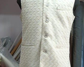 May include: Ivory-colored, sleeveless waistcoat with a textured, geometric pattern. Features a mandarin collar, three buttons, and two front pockets. The waistcoat is displayed on a black mannequin. The text "Sifatart" is visible on the bottom right.