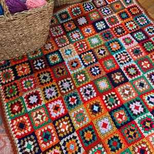May include: A colorful crocheted blanket with a granny square pattern in shades of red, orange, yellow, green, blue, and brown.