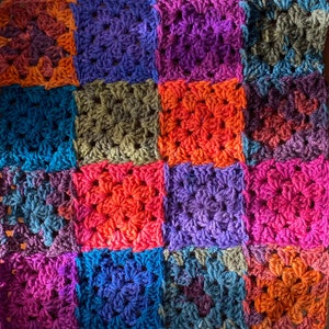 May include: A colorful crocheted blanket with squares in shades of purple, blue, green, orange, and brown.