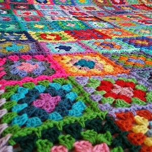 Op de afbeelding: Een kleurrijk gehaakt deken gemaakt van vierkanten in verschillende kleuren, waaronder roze, rood, groen, blauw en geel.