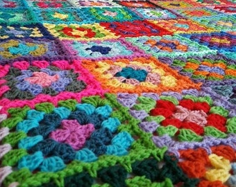 Op de afbeelding: Een kleurrijk gehaakt deken gemaakt van vierkanten in verschillende kleuren, waaronder roze, rood, groen, blauw en geel.