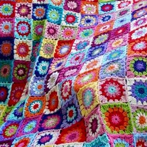 Könnte beinhalten: Eine farbenfrohe, handgefertigte Häkeldecke. Die Decke besteht aus zahlreichen quadratischen Motiven, die jeweils ein Blumendesign in einer Vielzahl von leuchtenden Farben wie Rot, Orange, Gelb, Grün, Blau und Lila aufweisen. Die Decke ist ein Patchwork aus verschiedenen Quadraten.