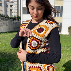 Könnte beinhalten: Eine gehäkelte Weste mit einem geometrischen Muster in Braun-, Orange-, Weiß- und Rottönen.