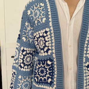 Könnte beinhalten: Blau-weiße Häkeljacke mit geometrischem Muster. Der offene Pullover hat ein quadratisches Design mit Blau- und Weißtönen. Die Strickjacke ist aus weichem, strukturiertem Garn gefertigt und hat eine lockere Passform.