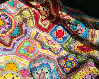 Puede incluir: Una manta de ganchillo colorida con un patrón geométrico de flores y cuadrados. La manta está hecha con una variedad de colores brillantes, incluyendo rojo, amarillo, azul, verde y morado.