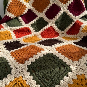 Pu&ograve; includere: Una coperta all'uncinetto fatta a mano con un design patchwork. La coperta presenta quadrati in vari colori, tra cui crema, arancione, giallo, verde e bordeaux, con un bordo color crema. La coperta &egrave; realizzata in morbido filato.