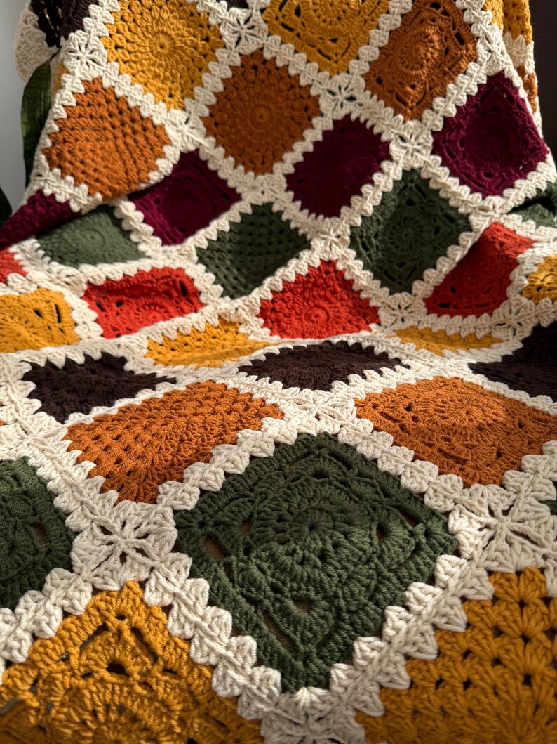 Pu&ograve; includere: Una coperta all'uncinetto fatta a mano con un design patchwork. La coperta presenta quadrati in vari colori, tra cui crema, arancione, giallo, verde e bordeaux, con un bordo color crema. La coperta &egrave; realizzata in morbido filato.