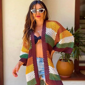 May include: A multi-colored crochet cardigan with brown, green, white, and yellow stripes. The cardigan is open in the front and has long sleeves.