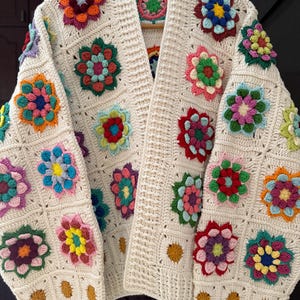 Puede incluir: C&aacute;rdigan de crochet color crema, abierto por delante, adornado con aplicaciones florales coloridas. Las flores presentan tonos de rojo, rosa, amarillo, azul y verde. El c&aacute;rdigan est&aacute; hecho de un hilo suave y texturizado y tiene un corte holgado.