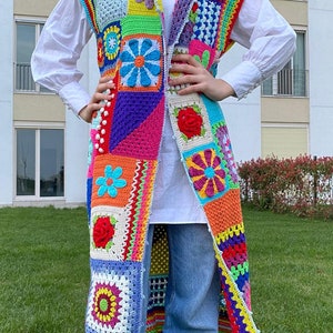 May include: A long, colorful crochet vest with a patchwork design featuring various floral motifs. The vest is sleeveless and has a deep V-neckline.