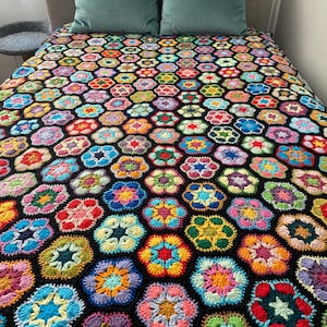 May include: A colourful crocheted blanket with a black background and a hexagonal pattern. The blanket is made up of many different coloured flowers.