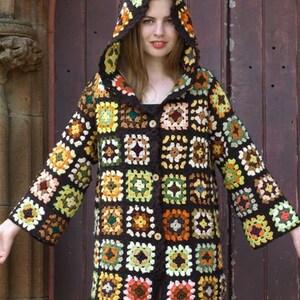 May include: A brown crocheted hooded cardigan with a colorful geometric pattern. The cardigan has a button closure and long sleeves.