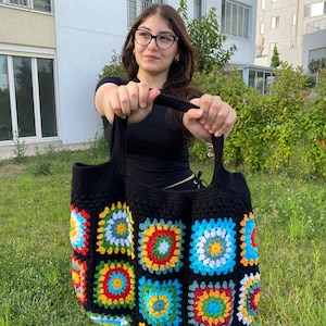 May include: A black crochet tote bag with colorful granny square patches. The bag has a wide, flat base and two short handles.