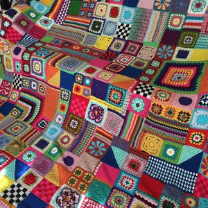 May include: A colourful, handmade crochet blanket with a patchwork design. The blanket features a variety of squares and shapes, including floral and geometric patterns. The colour palette includes shades of pink, blue, green, yellow, and orange.