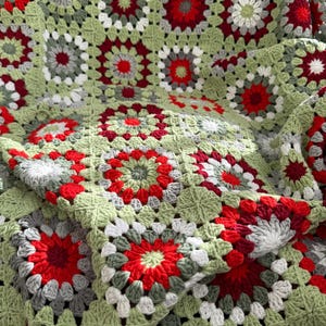 Può includere: Una coperta all'uncinetto fatta a mano con un motivo floreale nei toni del verde, rosso, grigio e bianco. La coperta è realizzata in filato morbido e ha un aspetto strutturato. Il design a quadrati granny aggiunge un tocco vintage a questo accogliente elemento d'arredo.
