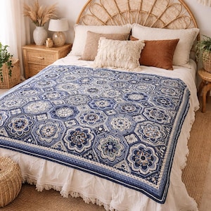 May include: A blue and white patterned crochet blanket with a floral design, displayed on a bed with a wicker headboard and neutral-toned pillows. The blanket's intricate pattern and colour palette create a cosy, inviting aesthetic. The bed is covered with a white bed skirt.