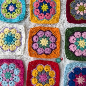 May include: Nine colorful, square crochet pieces arranged on a white, fluffy surface. Each square features a floral design in various colors, including blue, yellow, pink, orange, and green. The crochet work is detailed, with visible stitches and textured patterns.