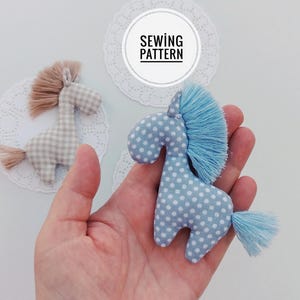 May include: Two handmade fabric horse toys. One is light blue with white polka dots, the other is tan and white checkered. Both have a fringe mane and tail. The image includes the text "SEWING PATTERN".