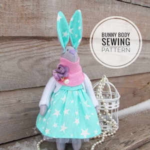 May include: A teal and white star patterned dress with a pink scarf and a white cardigan. The dress is on a stuffed bunny toy with teal ears and a gray face. The bunny is sitting on a wooden surface with a white pearl necklace and a white birdcage. The text "Bunny Body Sewing Pattern" is in a white circle.