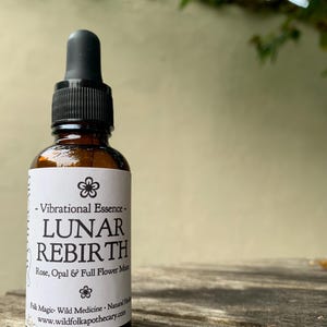 Op de afbeelding: Een bruine glazen fles met een zwarte druppelaar. Het etiket luidt "Vibrational Essence - LUNAR REBIRTH Rose, Opal & Full Flower Moon Folk Magic - Wild Medicine - Natural Healing www.wildfolkapothecary.com"