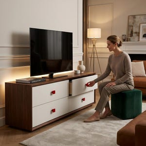 May include: A modern TV stand with a dark wood top and white drawers. The drawers have red square handles. A large black television sits on top. A woman is seated on a green ottoman, opening a drawer.