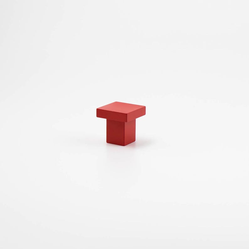 K&ouml;nnte beinhalten: Roter quadratischer Schrank-Knopf mit quadratischer Basis.
