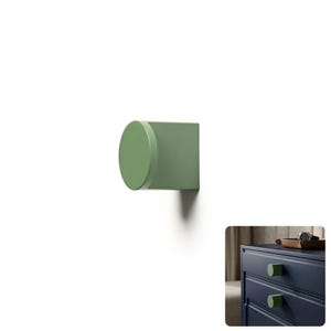 May include: A sage green cabinet knob featuring a circular front face and a square base. The knob is shown mounted on a dark blue drawer in the inset image, demonstrating its application as a functional piece of hardware for furniture.