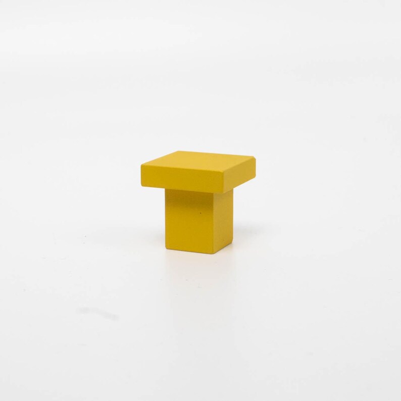 K&ouml;nnte beinhalten: Ein quadratischer gelber Schrank-Knopf mit quadratischer Basis.