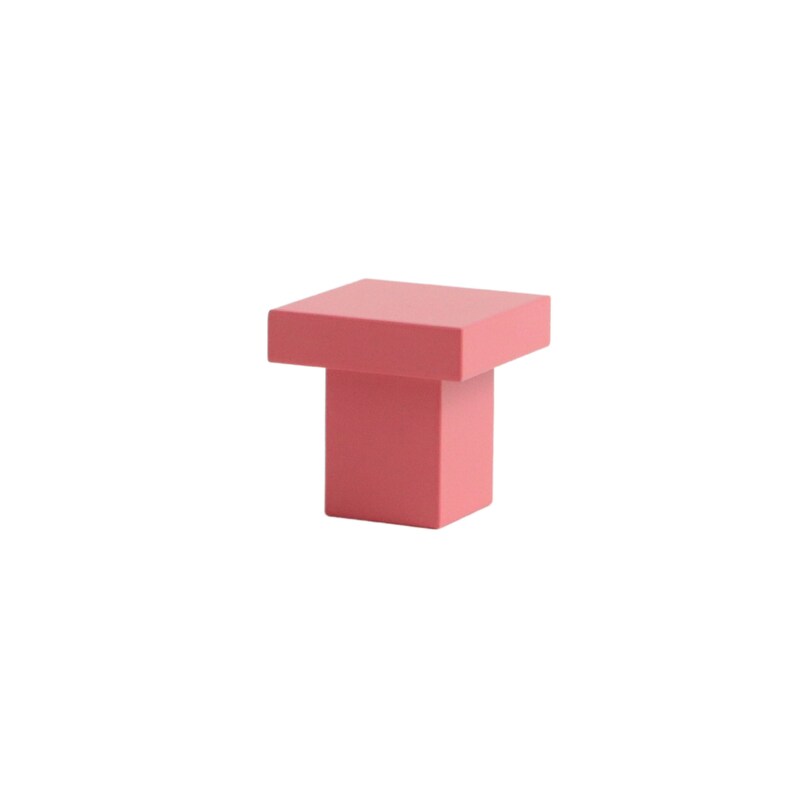 K&ouml;nnte beinhalten: Ein quadratischer rosa Schrank-Knopf mit quadratischer Basis.