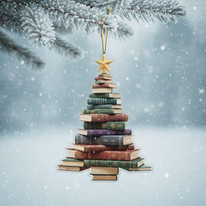 May include: A Christmas tree ornament shaped like a tree made of stacked books. The books are various colors, including green, red, and purple, and are topped with a gold star. The ornament hangs from a gold string against a snowy background.