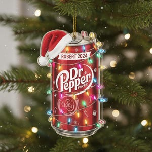 May include: A Christmas tree ornament shaped like a Dr. Pepper soda can, adorned with a Santa hat. The ornament is wrapped in colorful Christmas lights and features the text "ROBERT 2024" and the Dr. Pepper logo.