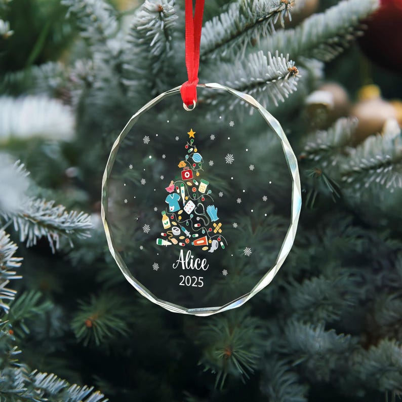 May include: A clear, round Christmas ornament with a red ribbon. The ornament features a Christmas tree design made of medical supplies and the name "Alice" and the year "2025".