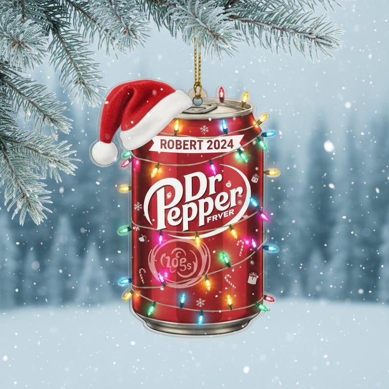 May include: A red Dr. Pepper can Christmas ornament with a Santa hat and string lights. The ornament has the text "ROBERT 2024" and "Dr. Pepper FRYER" on it. The ornament is hanging from a gold string.