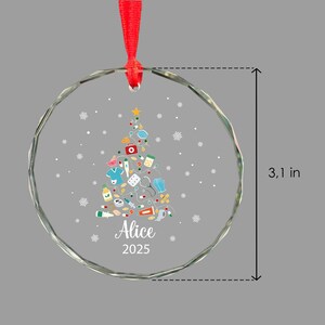 May include: A clear, round Christmas ornament with a red ribbon. The ornament features a Christmas tree design made of medical supplies and a star. The ornament is 3.1 inches in diameter and has the name "Alice" and the year "2025" printed on it.