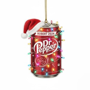 May include: A red Dr. Pepper can-shaped Christmas ornament with a Santa hat and string lights. The ornament has the text "ROBERT 2024" and "Dr. Pepper FRYER" on it. The ornament is a festive holiday decoration.