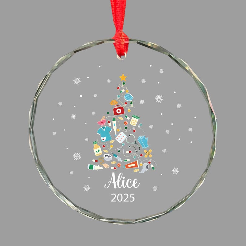 May include: A clear glass Christmas ornament with a red ribbon. The ornament features a Christmas tree design made of medical supplies and a star on top. The name "Alice" and the year "2025" are printed on the ornament.