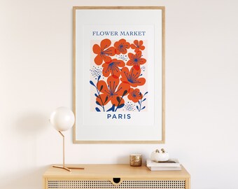 May include: A framed art print featuring a floral design with orange flowers and blue accents against a light pink background. The words "FLOWER MARKET" and "PARIS" are displayed in blue text. The print is in a light wood frame.