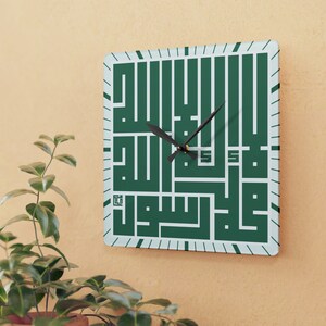 May include: Square wall clock with a green Arabic calligraphy design and black hands. The clock has a white background with a light blue border.