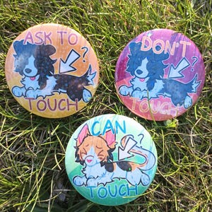 May include: Three circular pin badges with cartoon animal designs on grass. One reads "ASK TO TOUCH", another "DON'T TOUCH", and the third "CAN TOUCH". Each badge features a different animal and colour scheme.