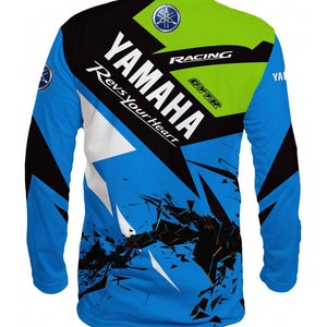 Puede incluir: Una camiseta de manga larga azul, negra, blanca y verde con un dise&ntilde;o gr&aacute;fico que presenta el logotipo de Yamaha y el texto "Yamaha Racing GYTR Revs Your Heart".