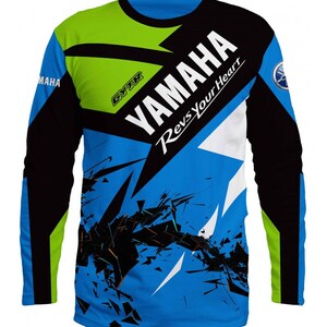 Puede incluir: Una camiseta de manga larga azul, negra, blanca y verde con un dise&ntilde;o gr&aacute;fico que presenta el logotipo de Yamaha y el texto "Yamaha Revs Your Heart".