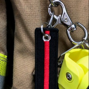 May include: A black and red keychain with a thin red stripe down the center. The keychain is attached to a silver metal carabiner.